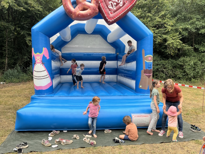 Kinder spielen auf und vor der blauen Hüpfburg.